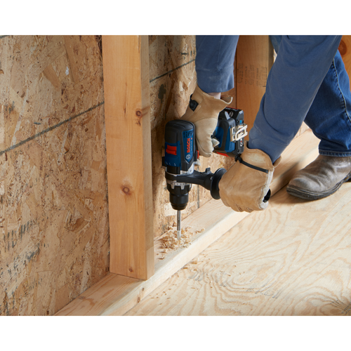 Bosch drill GSB18V-57C being used to drill a hole in wood, with wood shavings visible.