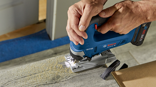 Bosch GST18V-50 cordless jigsaw in use, being held by a person over a wooden surface.