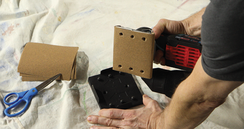 Person holding Bosch GSB18V-40 sander, with additional sandpaper and scissors on a cloth.