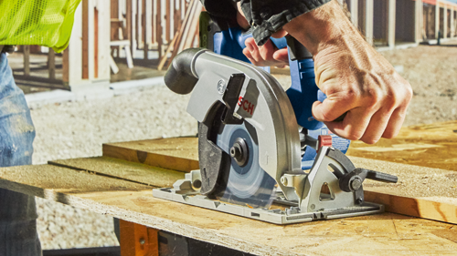 Bosch circular saw cutting a wooden board, held by a person.