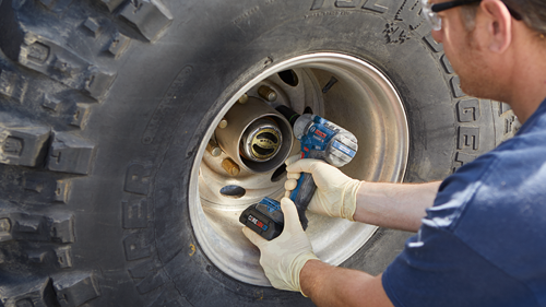 Bosch GDS18V-330PC cordless impact wrench with CORE18V battery being used on a wheel hub by a person.