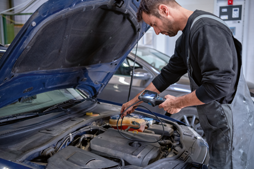 Mechanic using a diagnostic tool on a car engine.