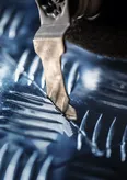 Close-up of a Bosch Starlock® Oscillating Multi-Tool carbide plunge cut blade in action, cutting through textured metal surface.