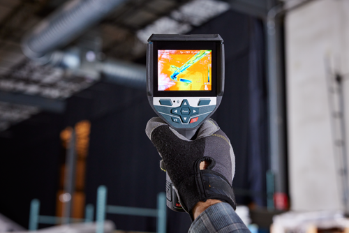 Bosch thermal imager displaying "10/04/2023 11:31:05am", "Tp=73°F E=0.95", and temperatures in Fahrenheit; held by a gloved hand.