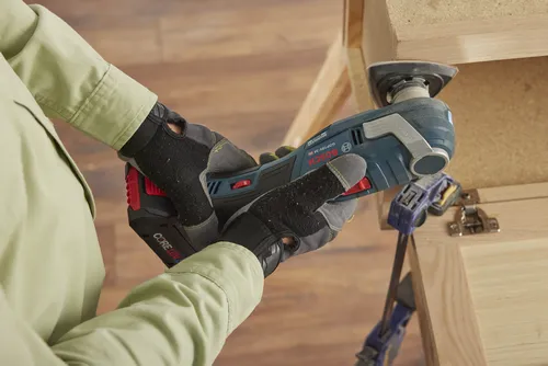 A person wearing gloves using a Bosch GOP18V-34 HD multi-tool on wood.