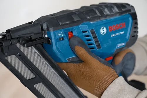 Bosch GNH18V-15MA nail gun, with red button and adjustment dial, held by gloved hand.