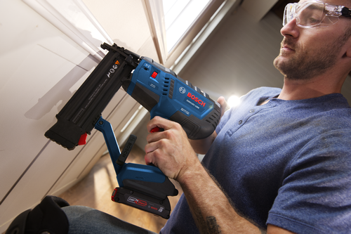 Bosch GNH18V-18M 18-GA BRUSHLESS MOTOR nailer being used by a person wearing safety glasses. The tool features “18ga Nail Capacity/Capacité du Clou/Capacidad de Clavos 5/8-2-1/8 in. (15-54 mm) (L)”