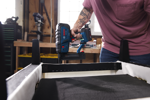 Bosch GTH18V-18M nail gun being used by a person wearing a pink shirt and jeans.