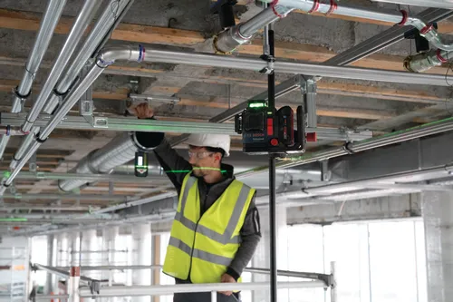 Construction worker wearing safety vest and hard hat, working with a Bosch GLL 3-80 CG Professional laser level.