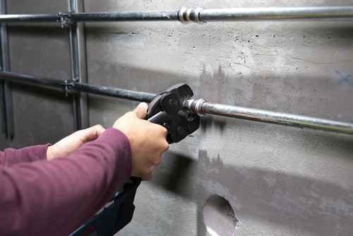 Person using a black Bosch tool to crimp metal tubing on a concrete wall.