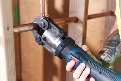 Bosch R-System P32 tool crimping a copper pipe, held by a person with a tattoo.