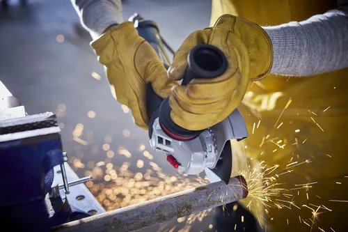 Person using an angle grinder to cut a metal rod, wearing yellow work gloves.