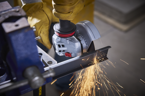 A person wearing yellow gloves is using an angle grinder to cut a metal beam. Sparks are flying.