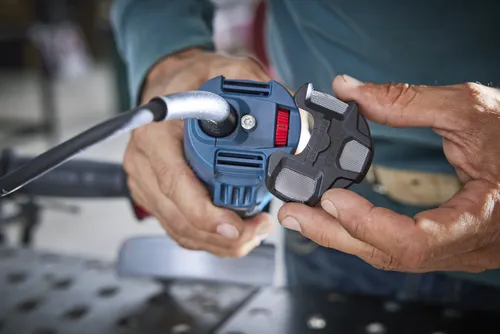 A person holding a blue power tool with a black attachment that has "KEEP CLEAN" and numbers "1 3 || 6" on it.