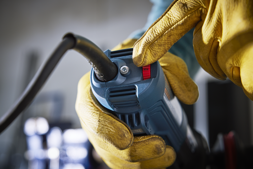 A person wearing yellow gloves adjusts the speed setting on a blue and black power tool with the number 2 visible.
