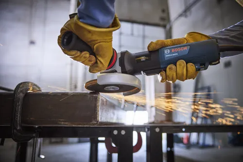 Bosch GWS14-60PD angle grinder, held by gloved hands, cutting metal with sparks flying.
