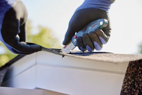 A person using the Bosch H11-11100-1 folding knife cutting a roofing material.
