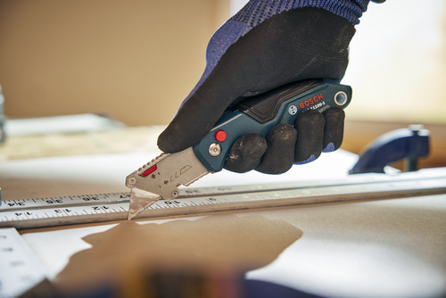 A person using the Bosch H11-11100-1 folding knife cutting a wood material.