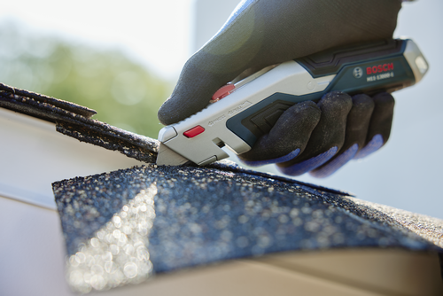 A person using the Bosch H11-13000-1 Retractable knife cutting a roofing material.