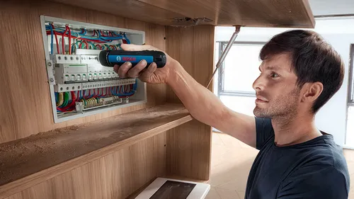 A technician using a Bosch GSD4V-35 rechargeable screwdriver to do repair on an electrical box.
