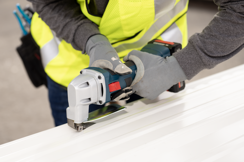 The worker using the Bosch GSC18V-16E 18V 16-Gauge Metal Shear with Lock- On Slide Switch to cutting a polycarbonate plate.