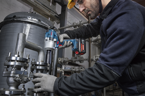 A worker is using a Bosch GDS18V-780 18V Brushless Mid-Torque Impact Wrench to tighten bolts on industrial pipes.
