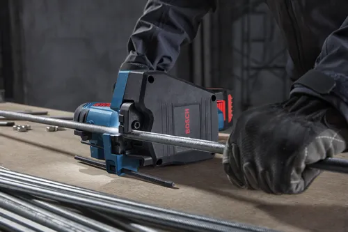 A worker is using a Bosch GGC18V-12 18V Brushless Threaded Rod Cutter to cut threaded metal rods on a workbench.