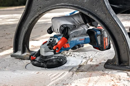The close-up image of worker using the Bosch GBR18V-15S 5 In. 18V Concrete Surface Grinder to grind a hard concrete floor.