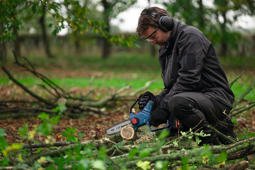 A worker using the Bosch GKE18V-20 18V Pruning Saw for cutting a small log of wood in a forest.