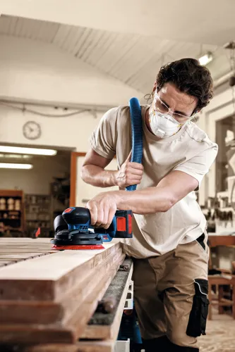 Image of worker using the Bosch EXEX18V-150-5N Random Orbit 18V 6” Random Orbit Sander (3/16”) for finishing a wooden strips.