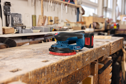 Image of Bosch GEX18V-150-3N 18V 6” Random Orbit Sander (3/32”) under a thick wooden board in a workshop.
