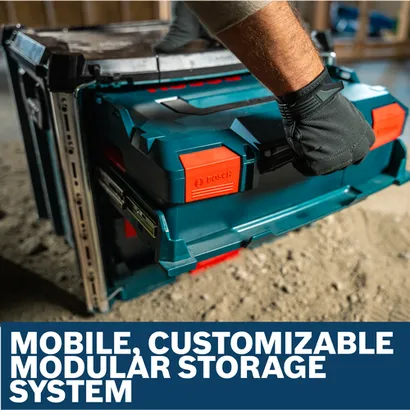Worker wearing gloves lifts a blue and red Bosch RACK-2 L-BOXX Contractor Rack on a dusty construction site.