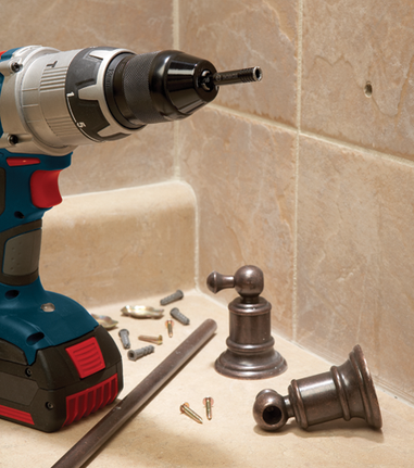 Bosch drill with a 13mm drill bit, drilling a hole in a tile wall, with other hardware and bathroom fixture parts visible.