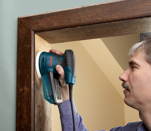 Bosch orbital sander, used by a person to sand a wooden frame.