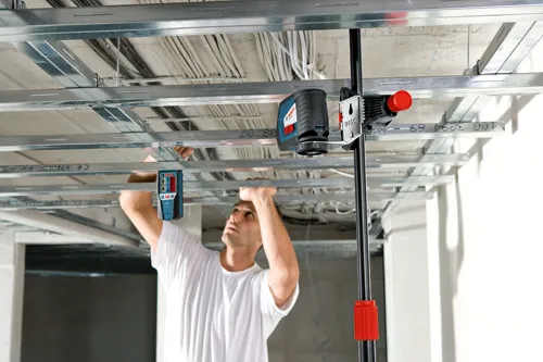 Man installing a laser level under metal ceiling beams, with a Bosch laser level attached to a pole.