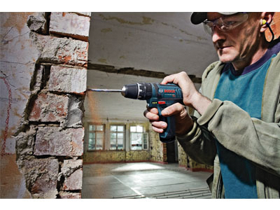 Perceuse Bosch utilisée sur un mur de briques, avec une personne portant une protection oculaire.