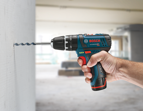 Perceuse Bosch Lithium-Ion 12V utilisée pour percer un trou dans un mur blanc. Le texte visible comprend "BOSCH", "LITHIUM-ION" et "15".