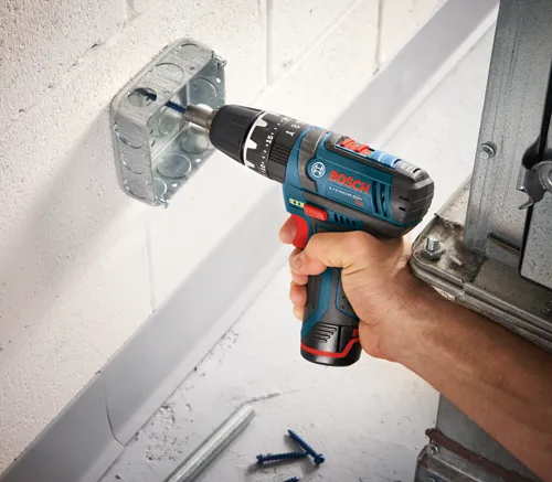 Perceuse Bosch Lithium-Ion utilisée pour visser dans une boîte de jonction métallique.