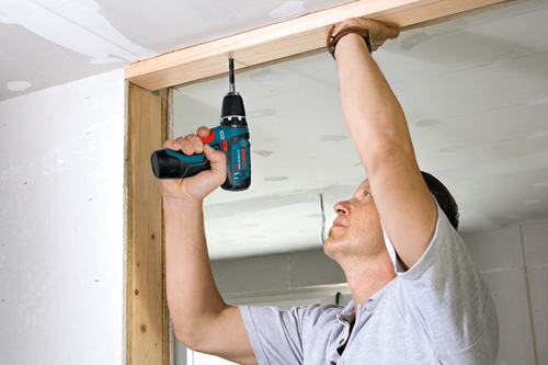 Homme utilisant une perceuse Bosch Lithium-Ion 12V pour installer un cadre en bois au plafond.