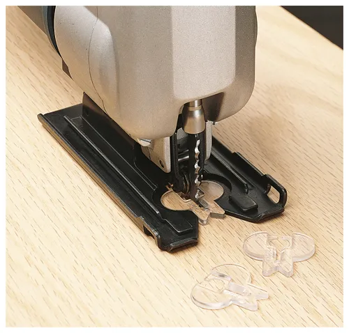 Une scie sauteuse coupant des pièces en plastique transparent sur une surface en bois.