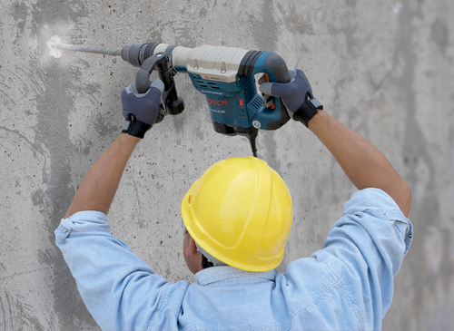 Voici la traduction :

Personne portant un casque de sécurité jaune utilisant un Boschhammer 11321EVS pour percer un mur en béton.