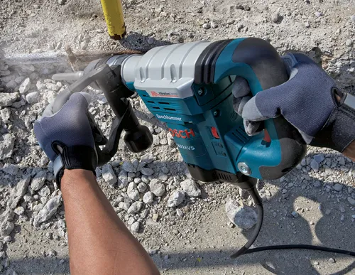 Marteau perforateur Boschhammer Bosch 11321EVS perçant du béton, tenu par des mains gantées.