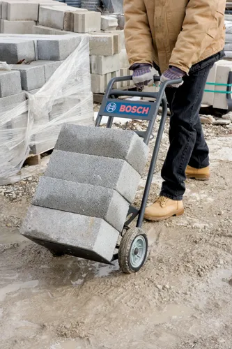 Voici la traduction:

Personne en tenue de travail tirant un diable portant la marque "BOSCH" et transportant des blocs de béton.