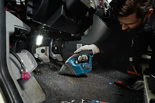 Homme nettoyant l'intérieur d'une voiture avec un aspirateur Bosch Lithium-Ion bleu et noir, portant des gants, dans une voiture.