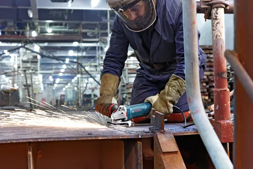 Voici la traduction :

Personne portant un équipement de protection individuelle utilisant une meuleuse d'angle Bosch, créant des étincelles.