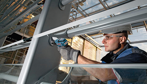 Voici la traduction :

Personne portant des lunettes de sécurité et un casque de protection, utilisant un outil électrique bleu et noir pour travailler sur une structure métallique.