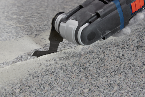 Lame BOSCH MATI 65 RT3 Carbide Grout+Abrasive coupant une surface en pierre.