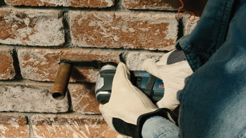 Perceuse Bosch utilisée sur un mur de briques, la perceuse est positionnée horizontalement.