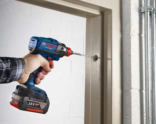 Perceuse Bosch Lithium-Ion 18V utilisée pour percer un trou dans une porte.