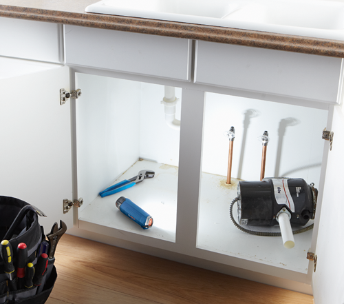 Voici la traduction :

Armoire de cuisine blanche ouverte avec des outils, une lampe de poche et un broyeur d'aliments InSinkErator 60S visibles.